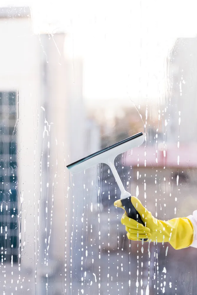 Eine Hand mit einem gelben Handschuh putzt ein Fenster